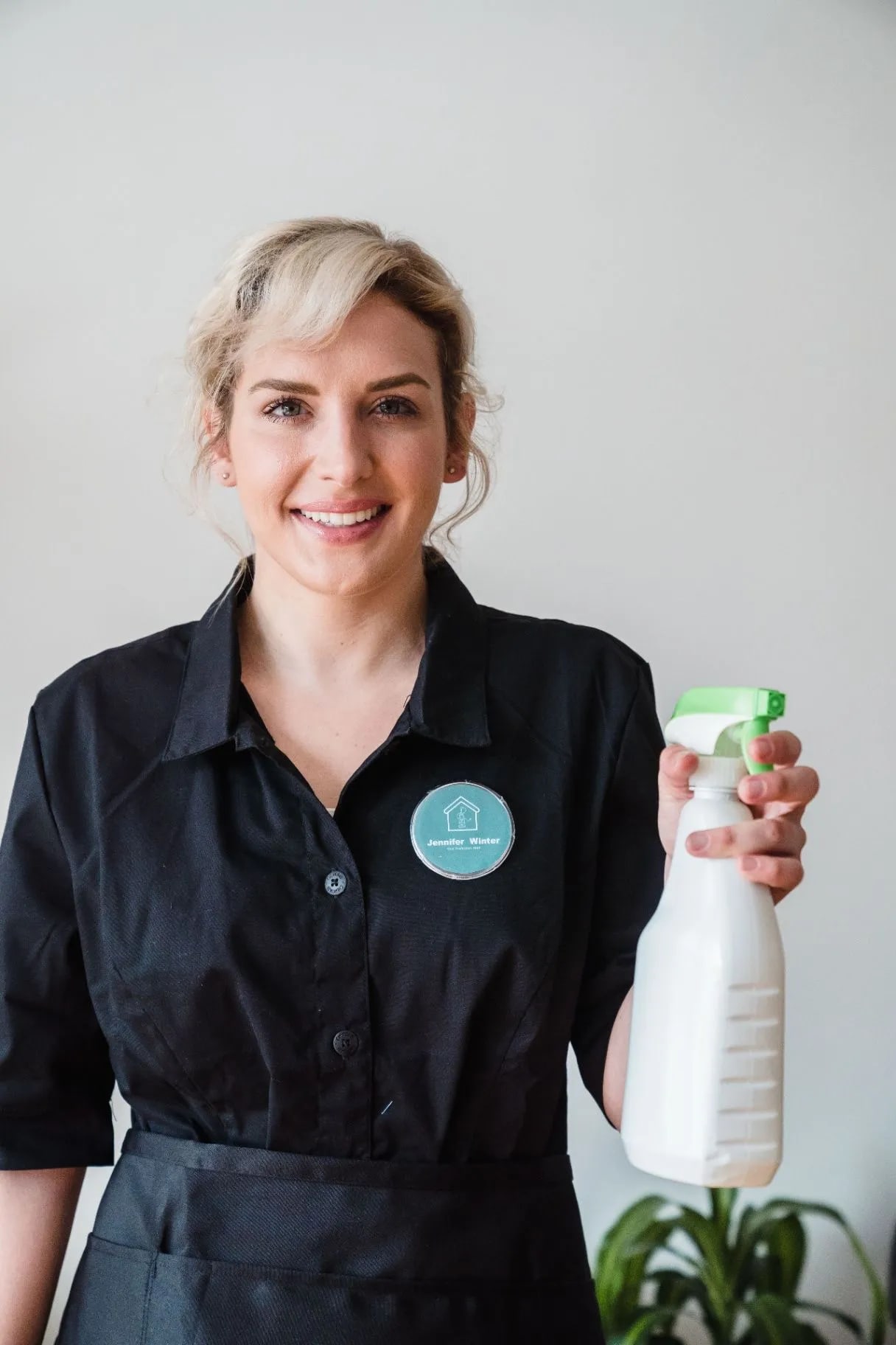 Smiling professional cleaner in a black uniform holding a spray bottle